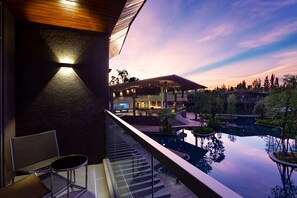 A modern outdoor pool area with a glass balustrade, a seating area with a chair and table, and a building with multiple lights in the background. - Kalima Resort & Villas Khaolak (Thai Mueang)