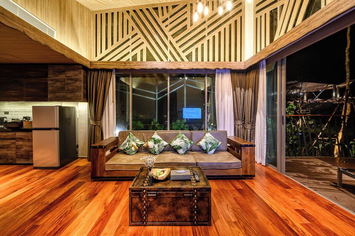 A modern living room with a wooden floor, a sofa with cushions, a coffee table, and a large window with curtains.