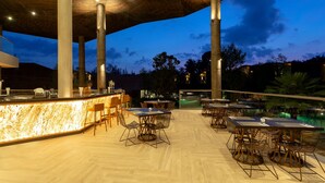 An outdoor dining area with tables and chairs, a bar, and a pool in the background. - Kalima Resort & Villas Khaolak (Thai Mueang)