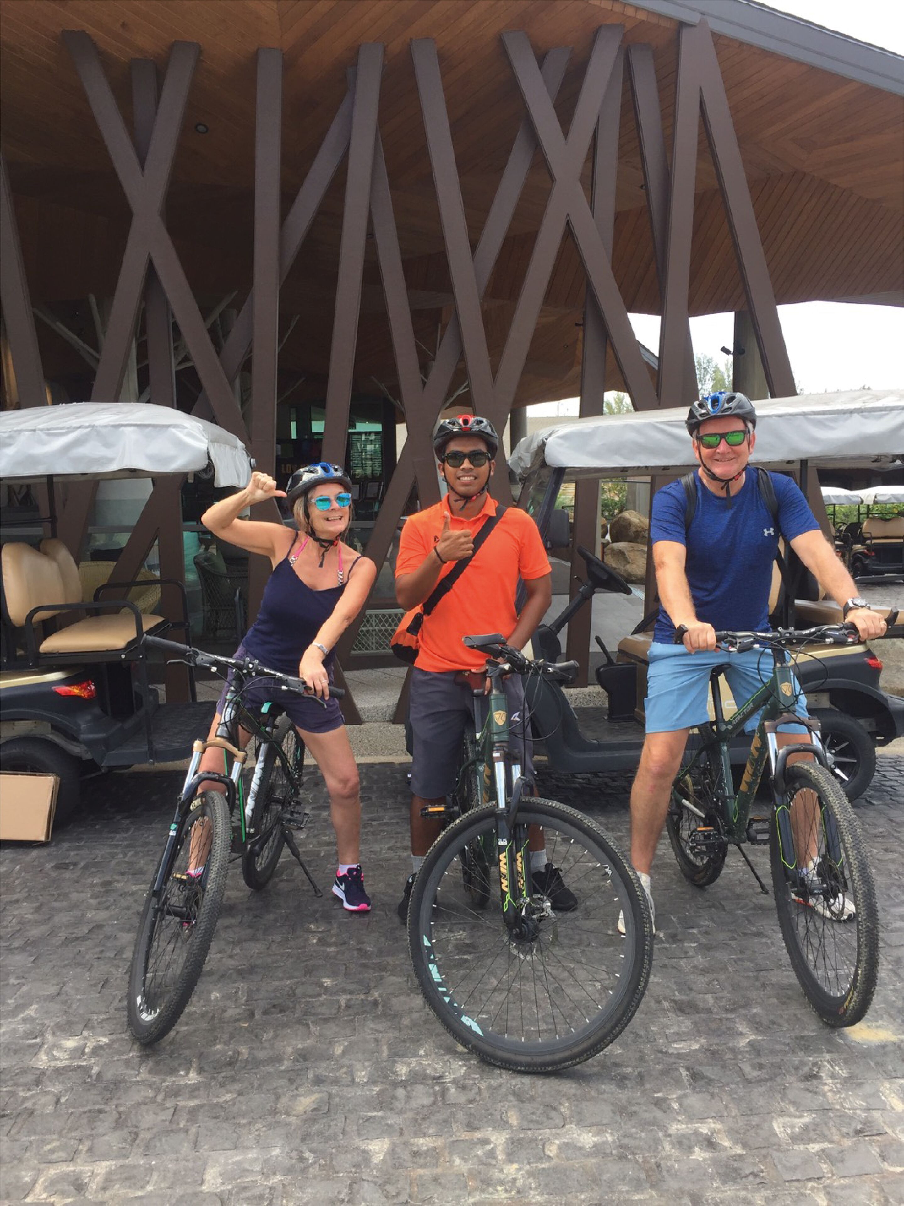 Three people with bicycles in front of a building with a distinctive wooden structure and outdoor seating.