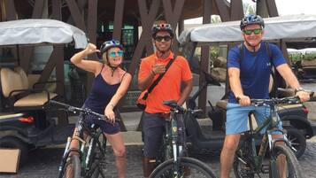 Three people with bicycles in front of a building with a distinctive wooden structure and outdoor seating.