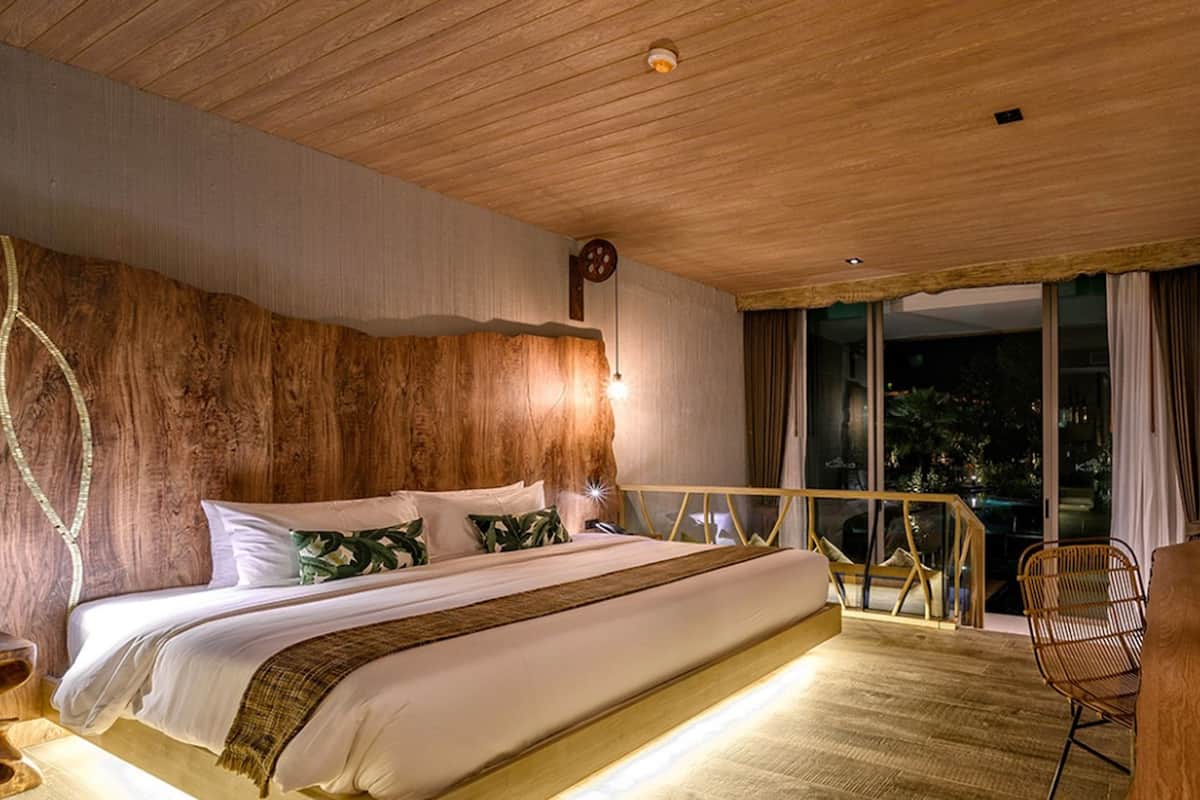 A modern bedroom with a wooden ceiling, a large bed, a bedside table, a chair, and a TV mounted on the wall.