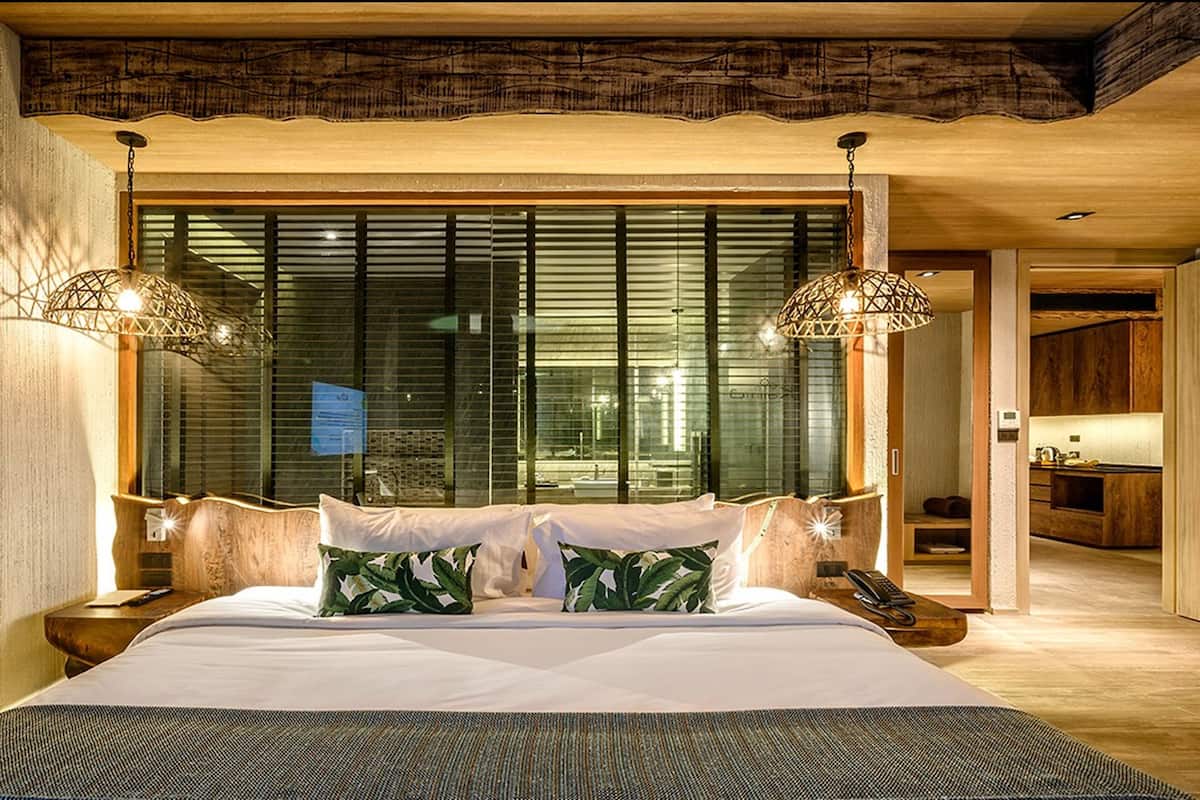 A modern bedroom with a large bed, two bedside lamps, and a view through floor-to-ceiling windows.