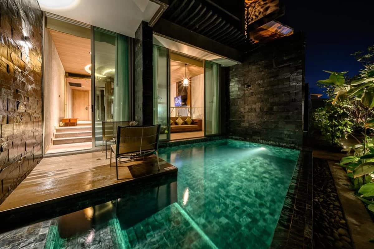 A modern outdoor pool area with a wooden deck, a seating area with a table and chairs, and a stone wall.