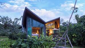 A modern house with a glass facade, a wooden deck, and a garden with large plants. - Kalima Resort & Villas Khaolak (Thai Mueang)