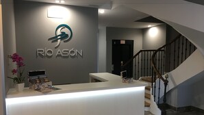 Eine Rezeption mit einem Logo und der Aufschrift 'RIO ASÓN' an der Wand, eine Treppe und eine Topforchidee.