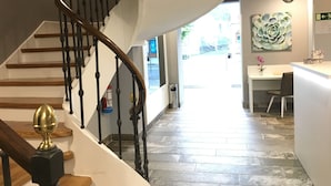 Eine Treppe mit hölzernem Geländer und schwarzen Spindeln führt zu einer Zwischenebene. Am oberen Ende der Treppe befindet sich eine dekorative Messingzierde.