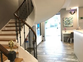 Una escalera de madera con barandilla y balaustradas negras que lleva a una plataforma. Un remate decorativo de latón se encuentra en la parte superior de la escalera.