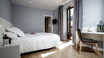 A modern bedroom with a bed, a desk, and a chair. There is a television on the wall and a window with curtains.