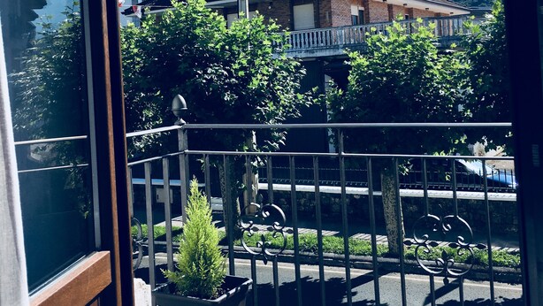 Ein Balkon mit Blick auf einen Berg, ein Haus und eine Straße mit parkenden Autos.