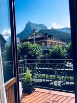 Un balcón con vistas a una montaña, una casa y una calle con coches estacionados.