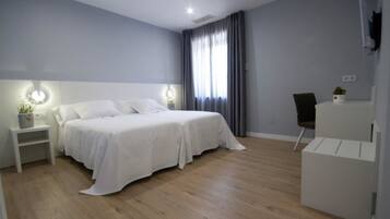 A modern bedroom with a double bed, bedside tables, a desk, and a chair.