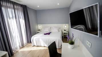 A modern hotel room with a large bed, bedside lamps, a desk with a chair, a potted plant, and a large mirror on the wall.