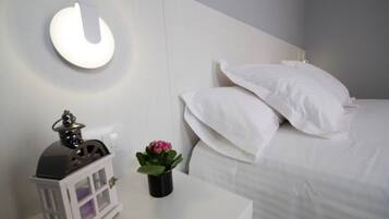A bedroom with a white bed, white nightstand, and a wall-mounted lamp.