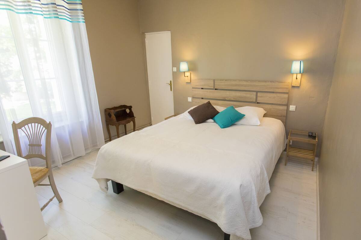 Une chambre à coucher bien rangée, avec un lit, des lampes de chevet, une chaise et un bureau.
