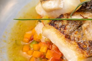 A close-up of a dish with grilled fish, diced vegetables, and a garnish. - Hôtel La Cauquière (Le Beausset)