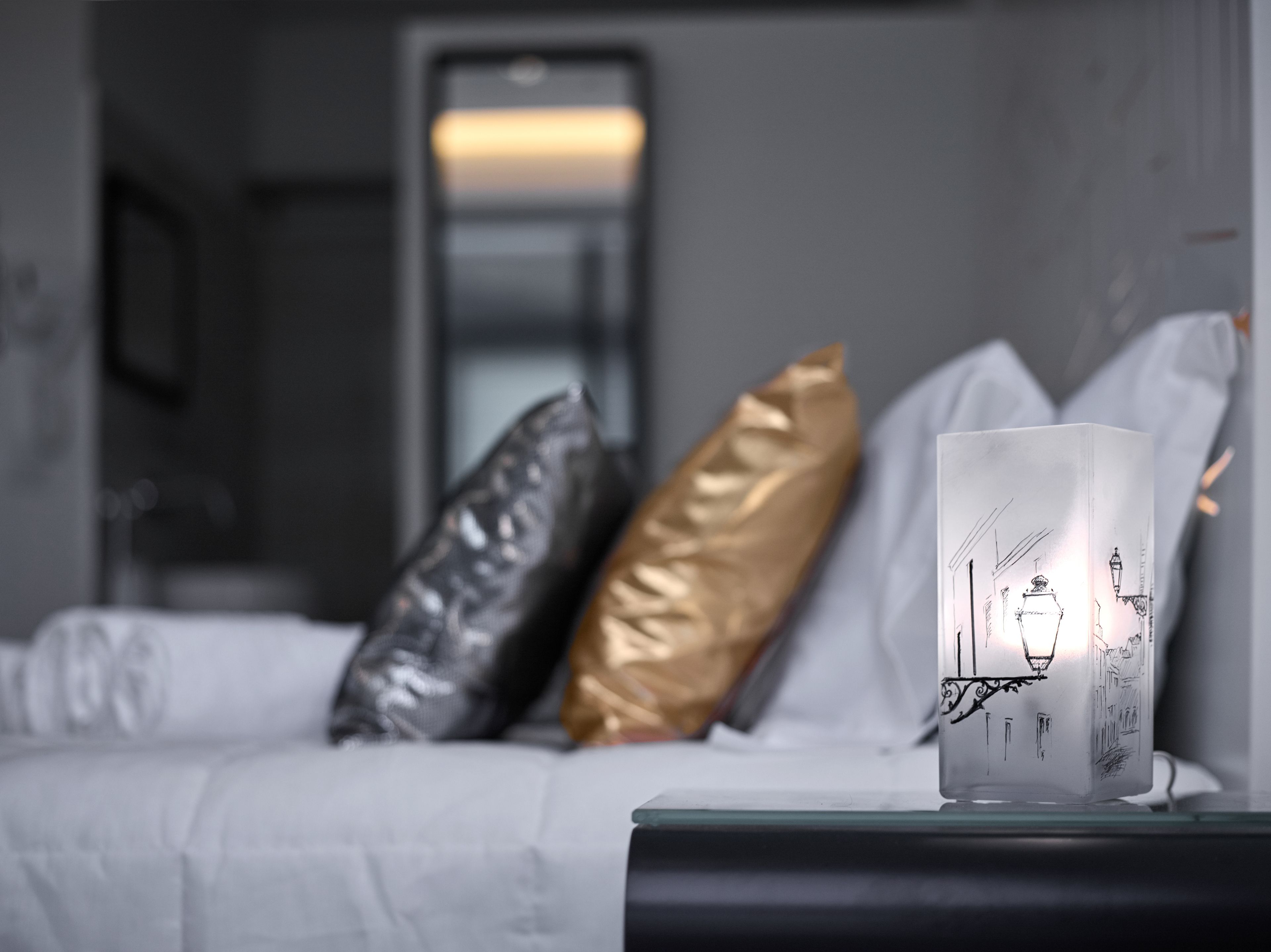 A neatly made bed with white linens, a bedside table with a lamp, and decorative pillows.