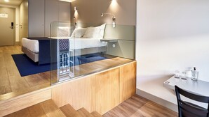 Een moderne hotelkamer met een glazen bed, een houten bureau en een klein tafeltje met glazen en een fles.