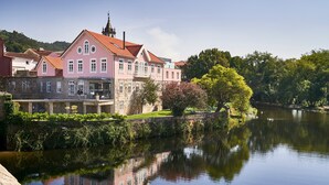 Een roze gebouw met een rood dak, een stenen muur en een reflectie in het water.