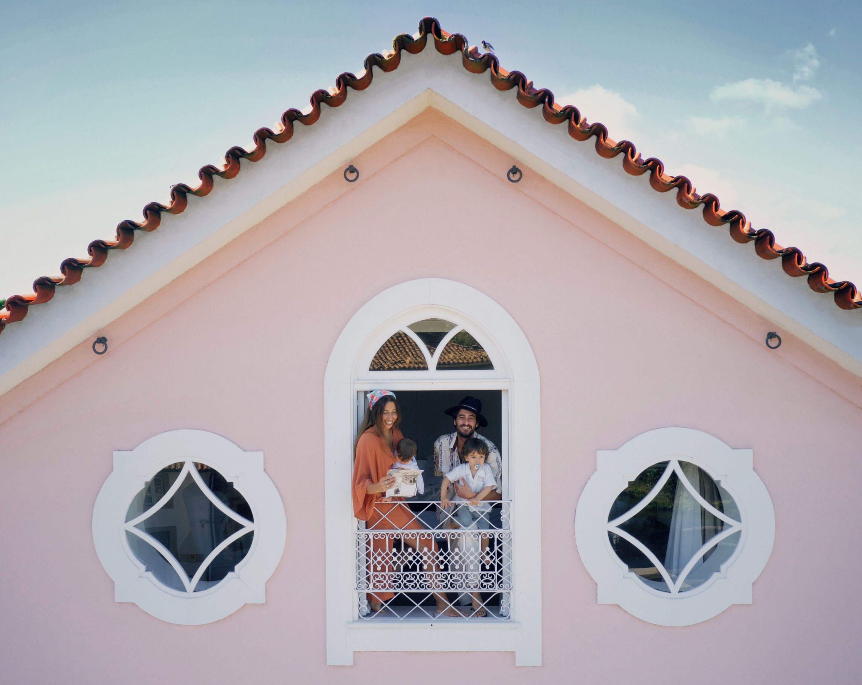 A pink building with a white window and balcony, a tiled roof, and decorative window frames.