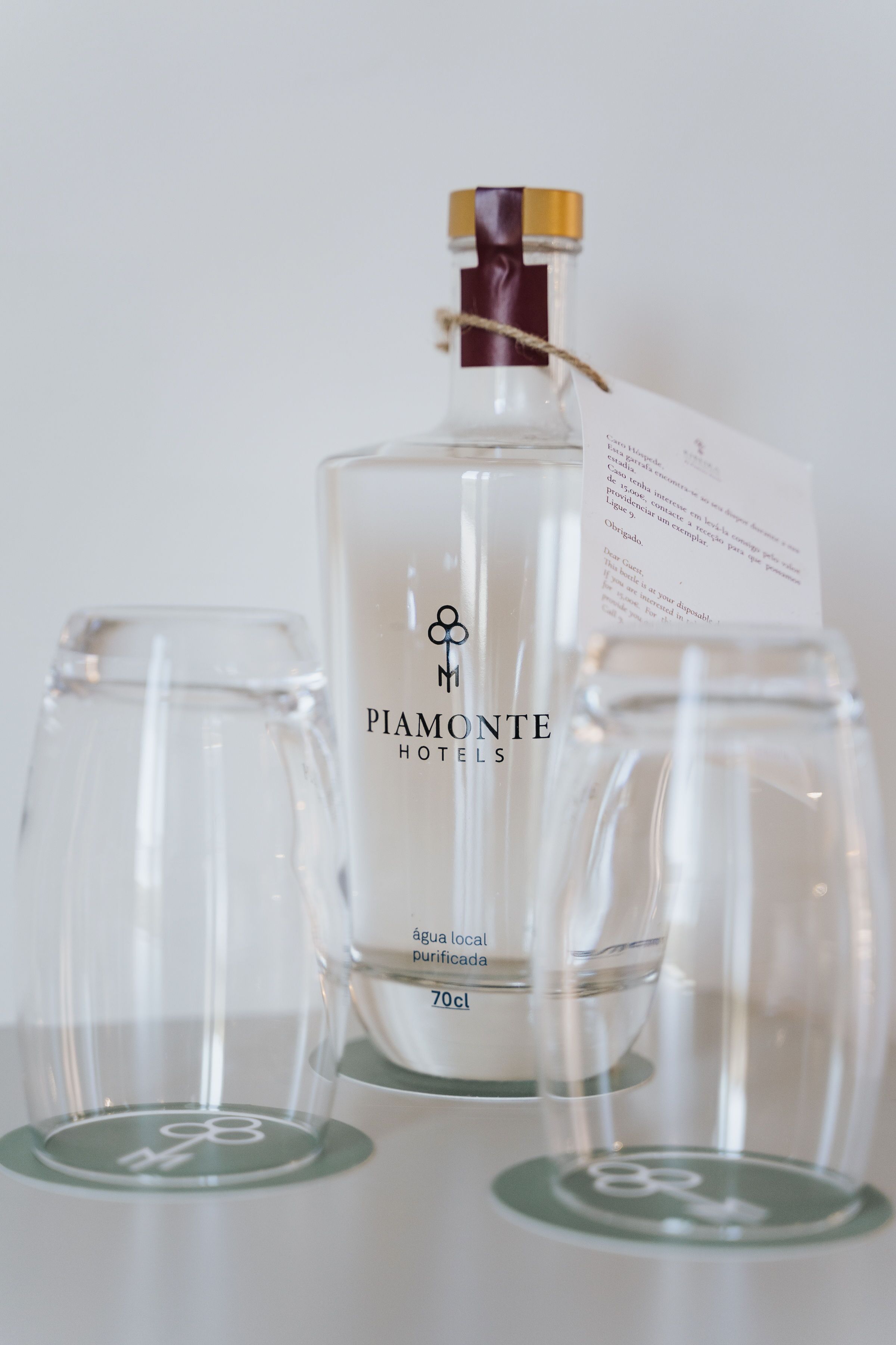 Une bouteille d’eau de source locale de l’hôtel Piamonte, 70 cl, accompagnée d’une étiquette et de deux verres vides.