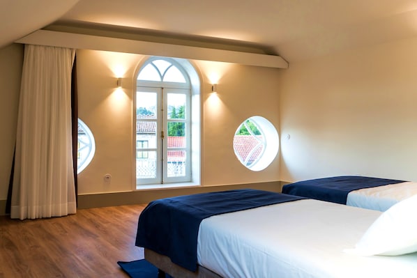 Un dormitorio con dos camas, un amplio ventanal de arco y dos luces fijadas a la pared.