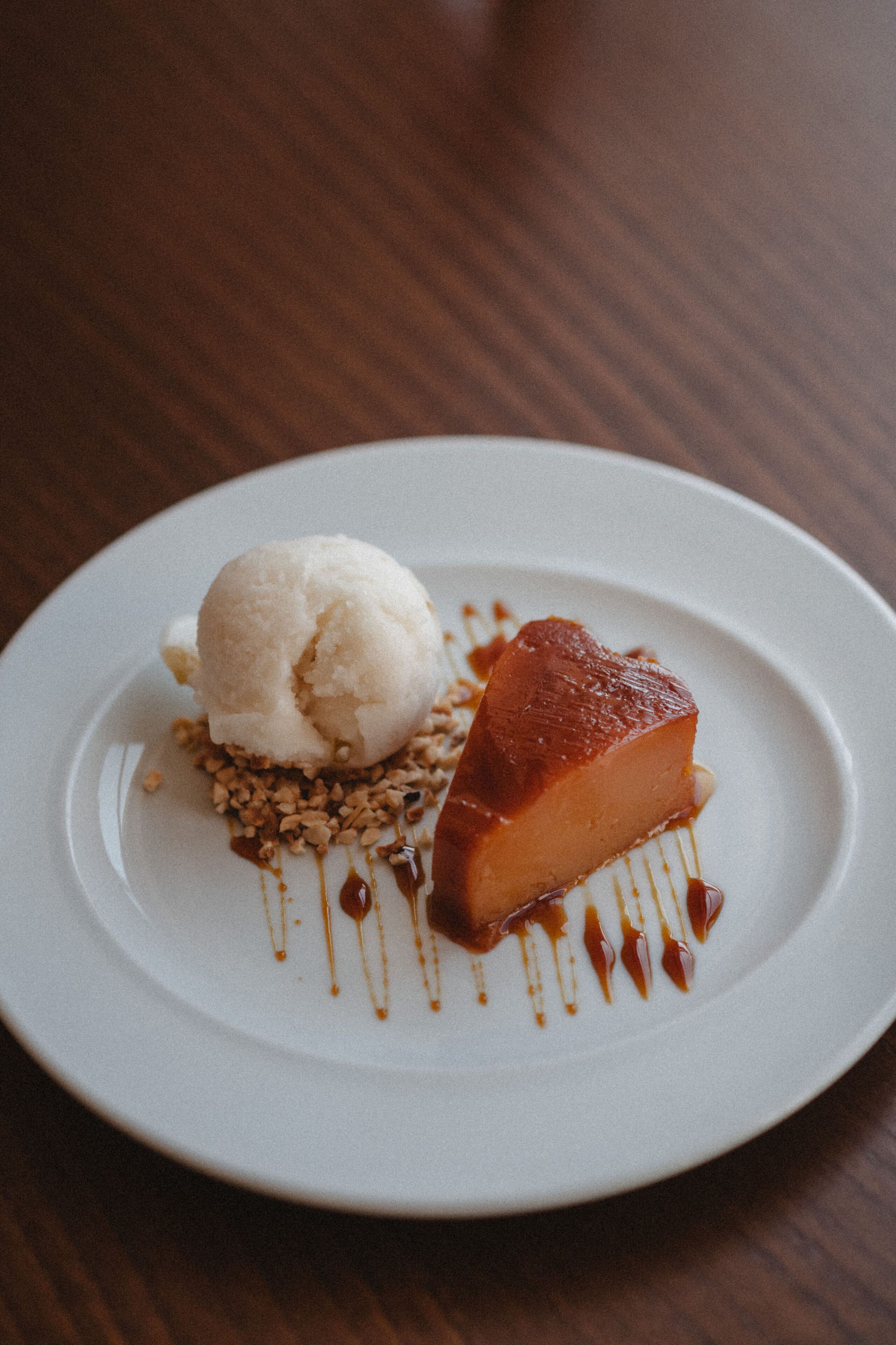 Une assiette de dessert avec une crème caramel et une boule de glace à la vanille, le tout présenté sur une assiette blanche.