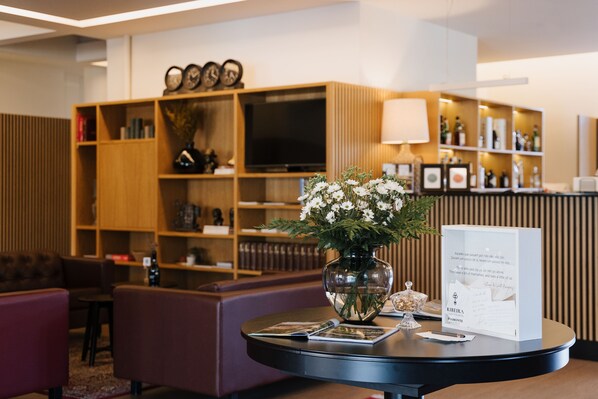 Un espace d’accueil comprenant une table ronde, un vase de fleurs, un panneau d’accueil encadré et une bibliothèque en bois contenant divers objets.