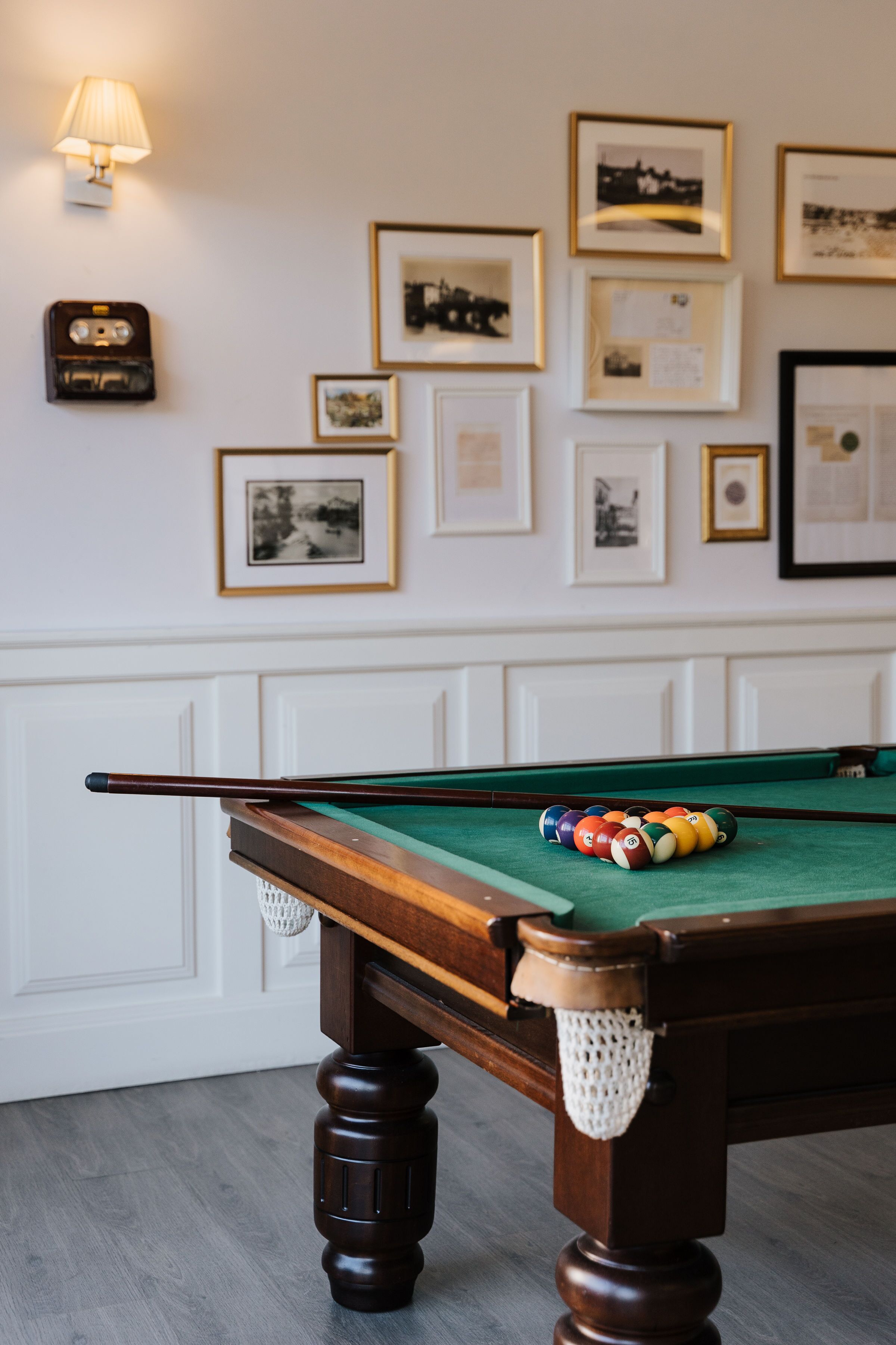 Une table de billard avec un queue, entourée de tableaux encadrés accrochés au mur.