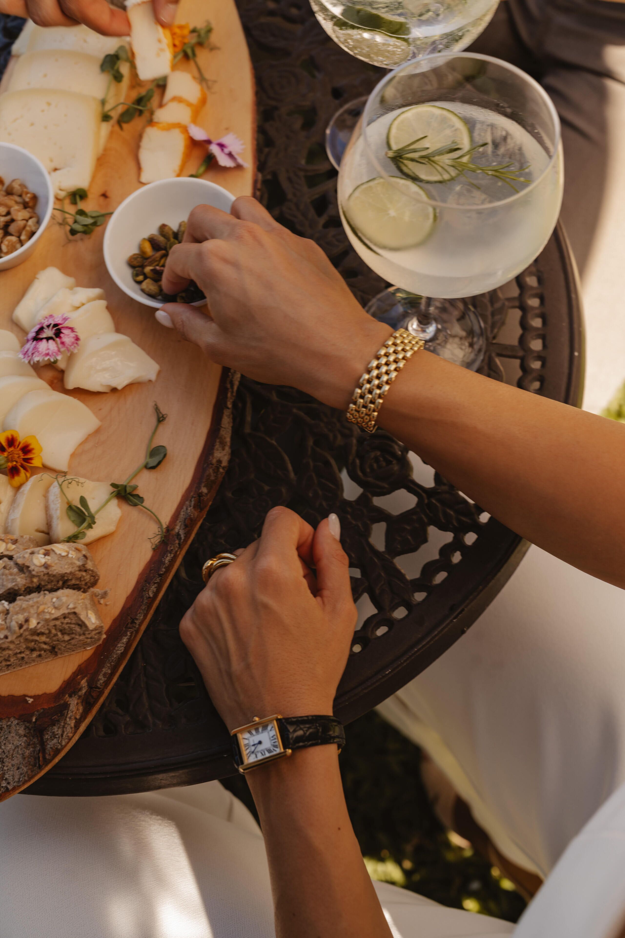 Una mesa con queso, frutos secos, flores y dos vasos de una bebida transparente con lima y romero.