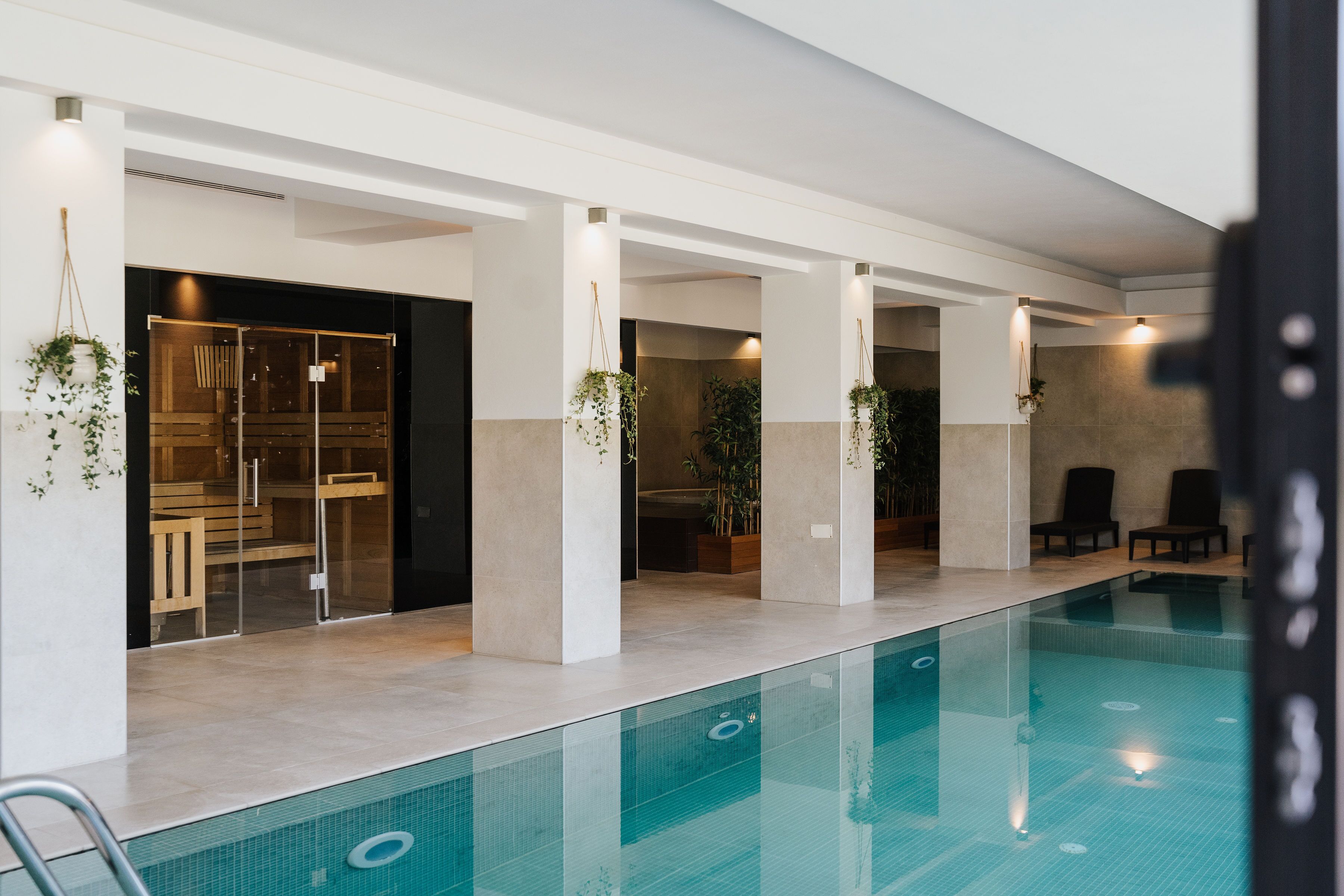 En modern inomhuspool med klart vatten, omgiven av vita pelare och krukväxter.