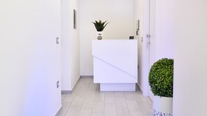 Un espace d’accueil moderne avec un comptoir de réception blanc, une plante en pot et une colonne décorative.