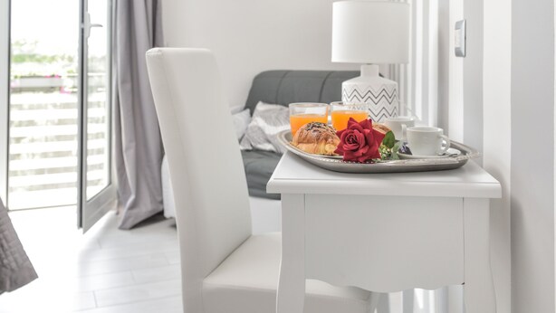 Une chambre moderne avec une table blanche dressée pour le petit-déjeuner, un téléviseur fixé au mur et une vue sur l’extérieur grâce à une porte coulissante.