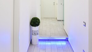 Un couloir moderne avec des murs blancs, une plante en pot et un bandeau lumineux à LED bleu.