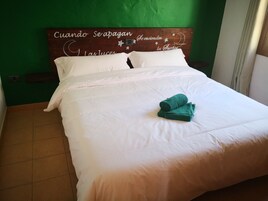 Una cama bien hecha con sábanas blancas y una toalla verde enrollada encima.
