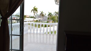 A view from a balcony with a white balustrade, palm trees, and houses in the background. - Waters Edge Condo With Boat Slip (Freeport)