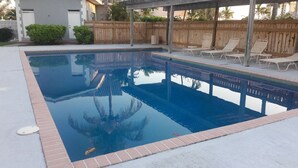A rectangular swimming pool with a wooden deck and lounge chairs. - Waters Edge Condo With Boat Slip (Freeport)