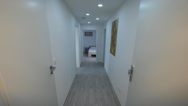 Un estrecho pasillo con paredes blancas y suelo de madera, que conduce a un dormitorio con una cama y un cuadro en la pared.