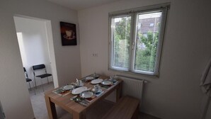 Un comedor con una mesa de madera preparada para cuatro, una ventana con persianas y un radiador.