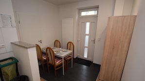 Un coin repas avec une table dressée pour quatre personnes, des chaises en bois, une poubelle et une porte avec une fenêtre.
