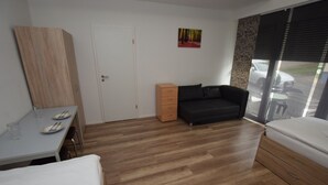 Une pièce avec un plancher en bois, un lit, un canapé, un bureau avec une chaise et une fenêtre donnant sur l’extérieur.