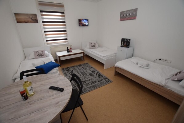 Habitación de hotel compacta con dos camas individuales, una mesita con una silla, televisión y ventana con persianas.