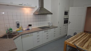 A modern kitchen with white cabinets, a stainless steel range hood, a built-in oven, and a dining area with a wooden table.