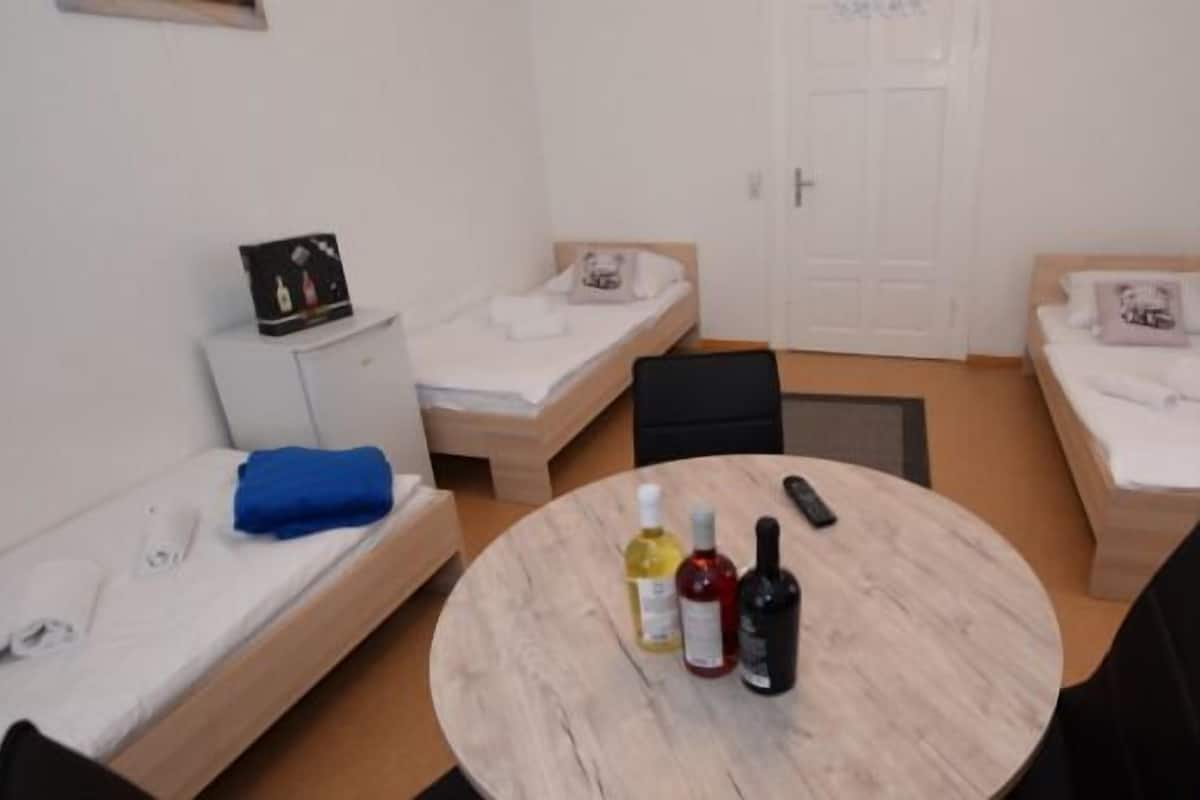 A small, clean room with two single beds, a round table with bottles, and a small cabinet.