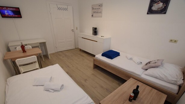 A small, tidy room with two single beds, a wooden table, a desk, and a TV mounted on the wall.