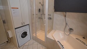 A bathroom with a glass-enclosed shower, a washing machine, and a bathtub.