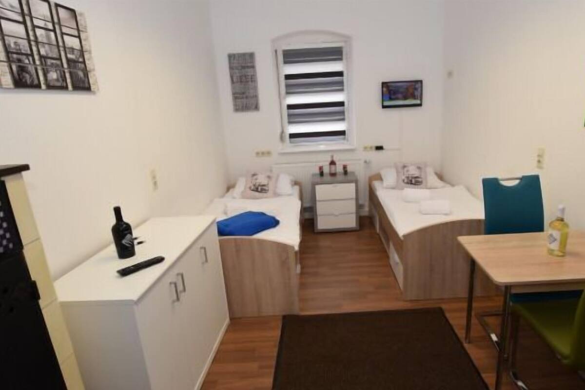 A compact room with a bed, a small table, a chair, a desk, and a wardrobe.