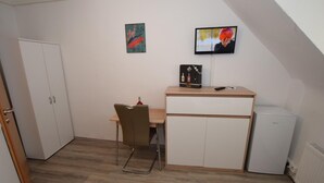 A small, compact room with a desk, chair, and a television mounted on the wall.