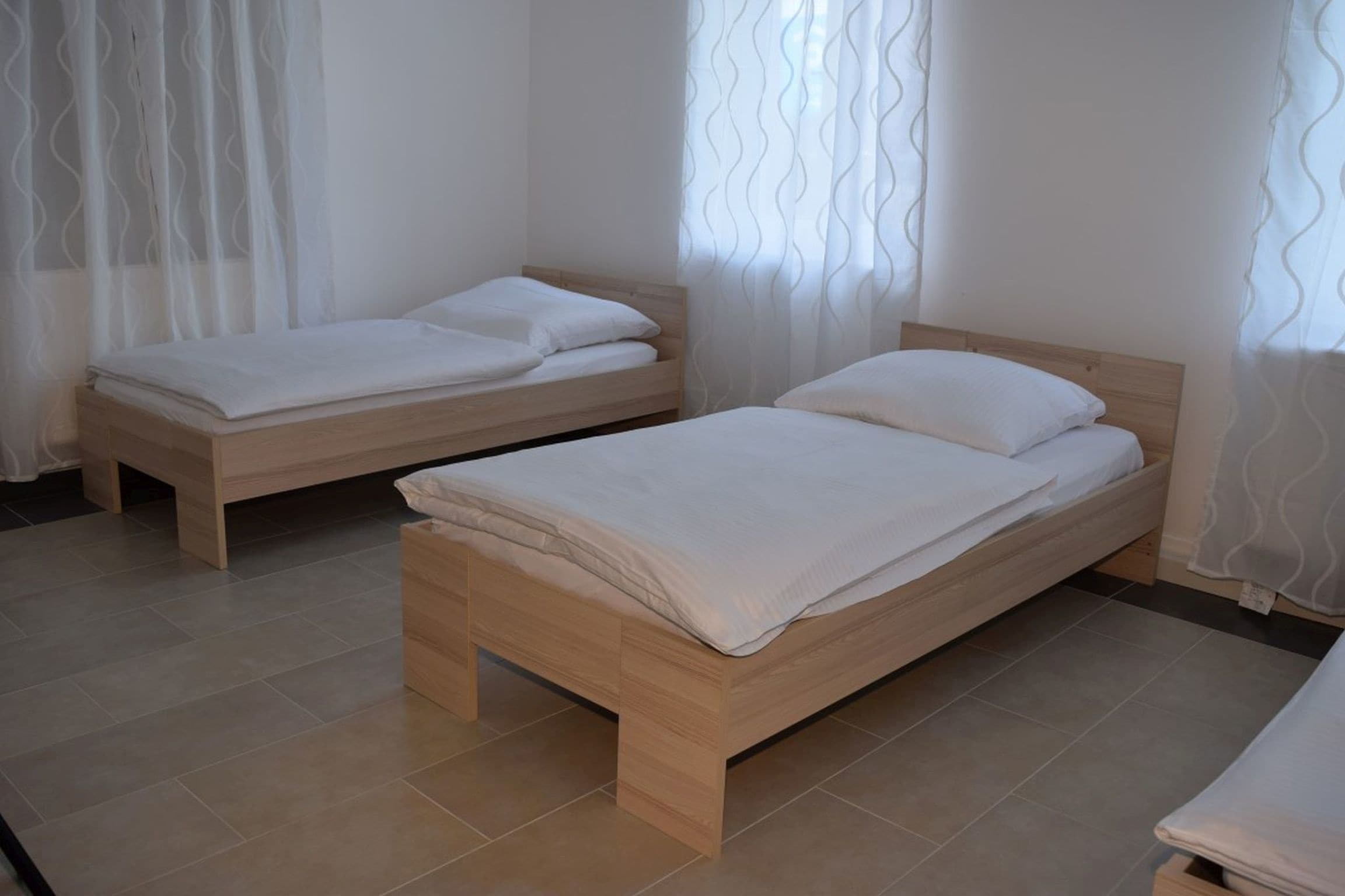 Una habitación con dos camas de madera, ropa de cama blanca y cortinas de encaje.