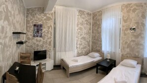 Une chambre d’hôtel avec trois lits, une télévision, un bureau et un tableau représentant la Tour Eiffel.